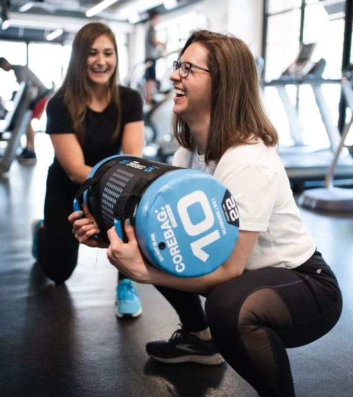 a gym member squats with weights while a personal trainer spots them at trophy fitness near me